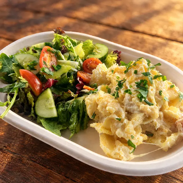 Kartoffelgratin mit geschmolzenem Käse und Kräutern, dazu gemischter Salat in der Pappschale auf Holz